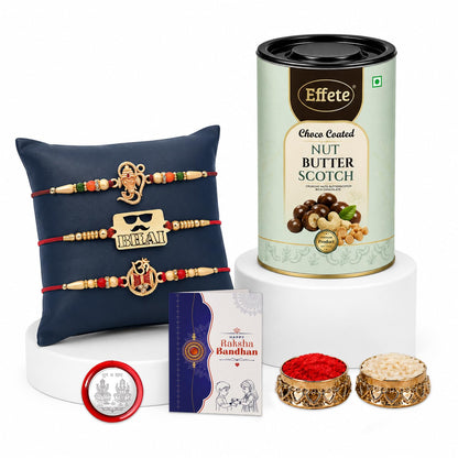 A Rakshabandhan gift set with three red and gold Rakhis on a dark blue pillow, a greeting card, a tin of chocolates, and two