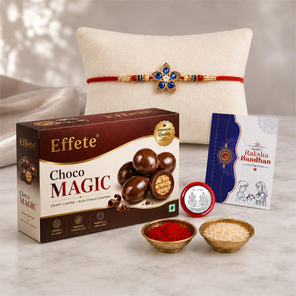 A Rakhi gift set includes a box of chocolates, a red and blue floral Rakhi on a white pillow, and small bowls of rice and
