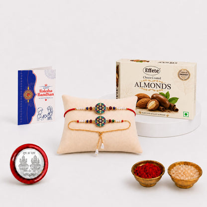 A Rakhi gift set on a white background includes two bracelets on a pillow, a box of chocolate almonds, a greeting card, a