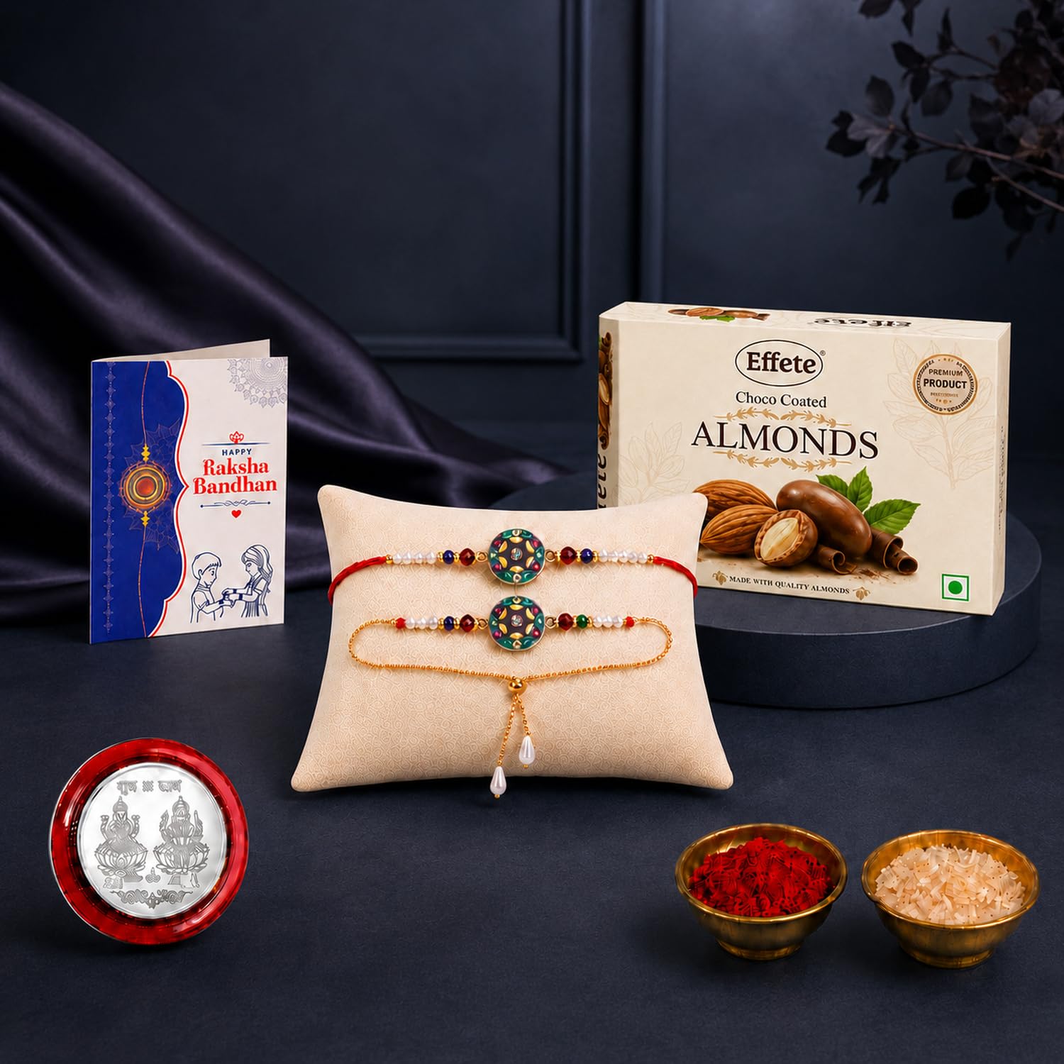 A Rakhi gift set on a dark surface features two colorful bracelets on a beige pillow, a box of chocolate almonds, a greeting