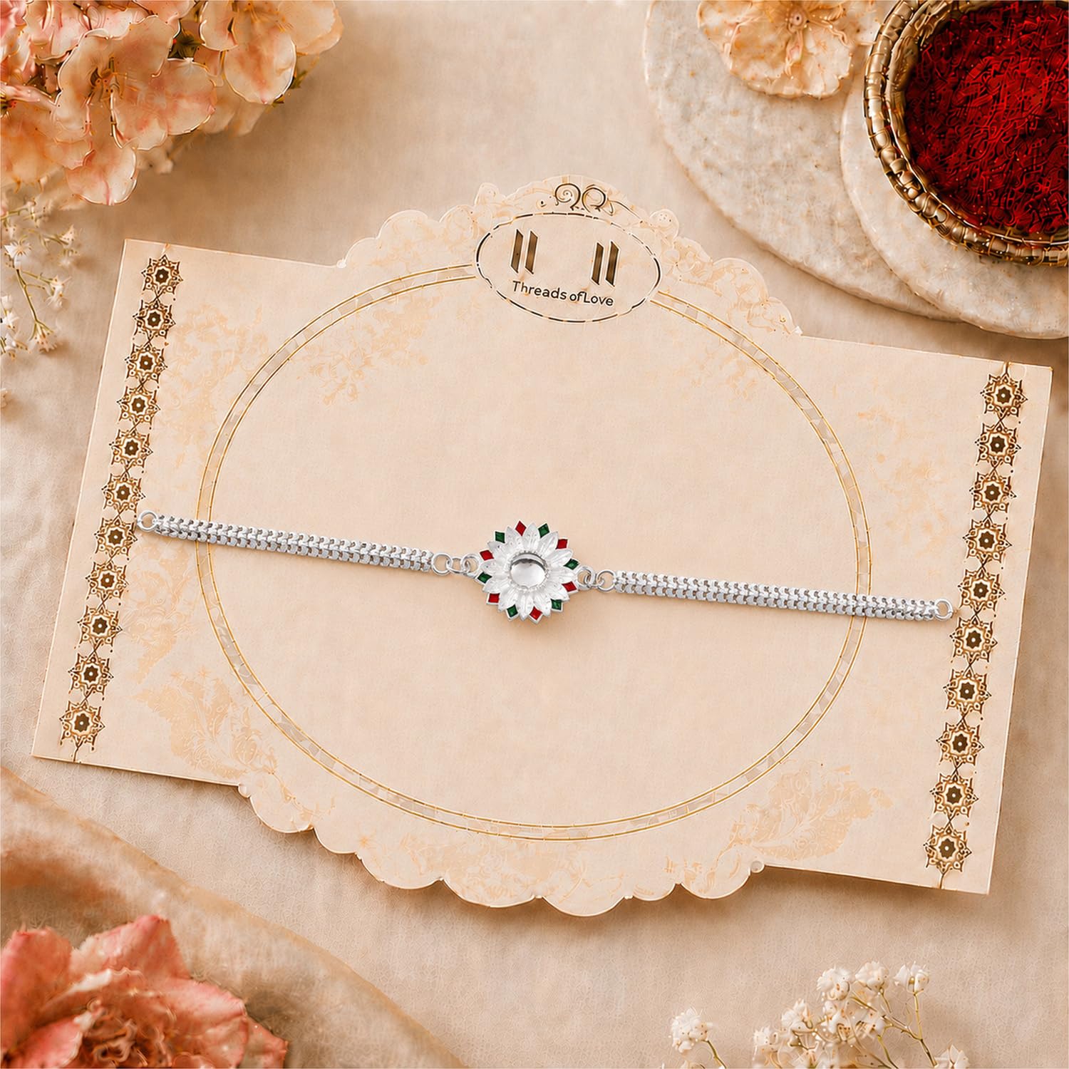 A silver-colored bracelet with a white, red, and green floral centerpiece is displayed on a decorative beige card with