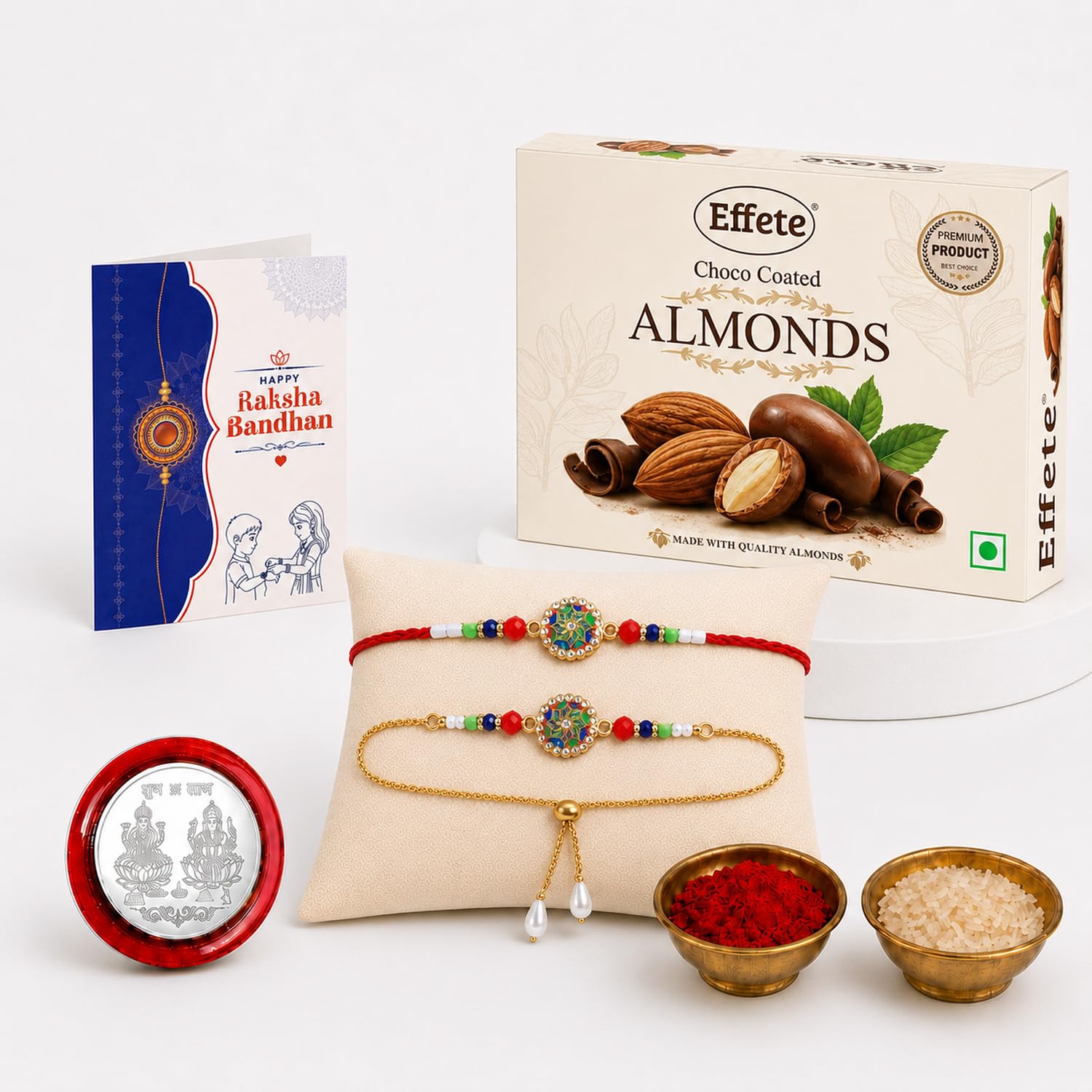 A gift set with two decorative bracelets, a box of chocolate almonds, a greeting card, and small bowls of rice and kumkum