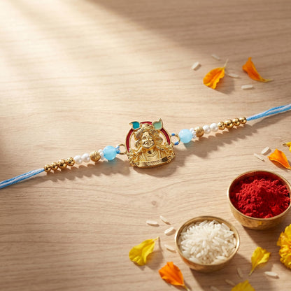 A light blue thread bracelet with a gold charm depicting a person's face and light blue and white beads is on a wooden