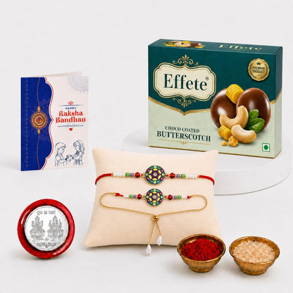 A Raksha Bandhan gift set with a greeting card, a box of chocolates, two bracelets on a pillow, a silver coin, and small