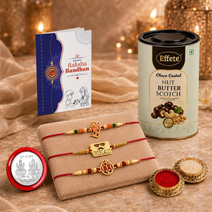 A Rakshabandhan gift set with three red and gold Rakhis on a beige pillow, a greeting card, a tin of chocolates, and two