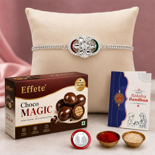 A silver bracelet with a red, green, and white oval centerpiece rests on a beige pillow, with chocolate, a greeting card,