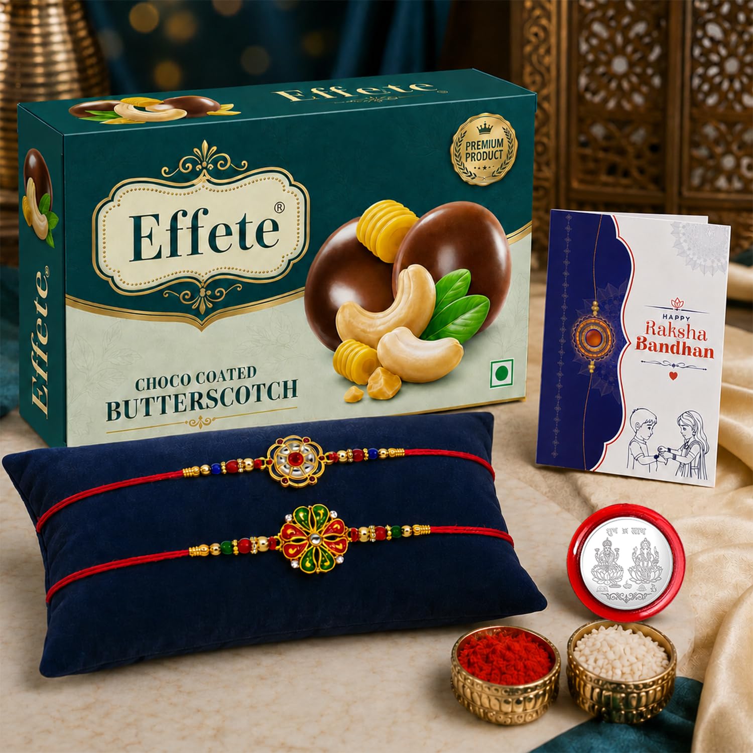 A teal box of Effete Choco Coated Butterscotch chocolates, two floral Rakhis on a blue cushion, a Raksha Bandhan card, and