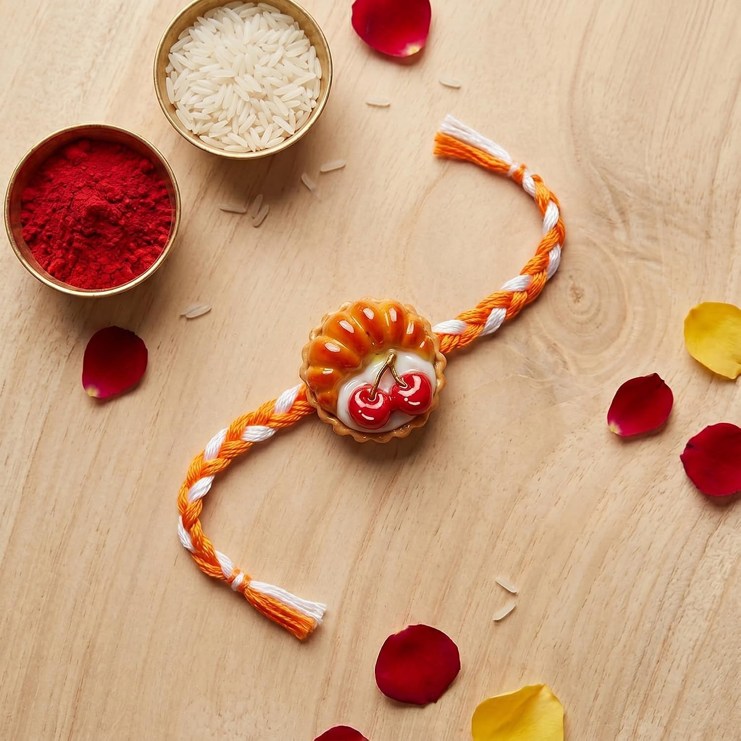An orange and white braided thread with a cherry pie charm is surrounded by red and yellow flower petals and small bowls of