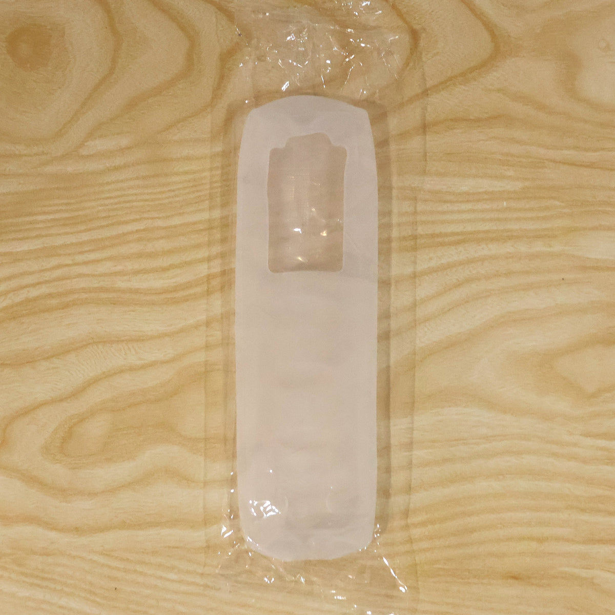 A clear silicone remote control cover is sealed inside transparent plastic packaging on a light wooden surface.