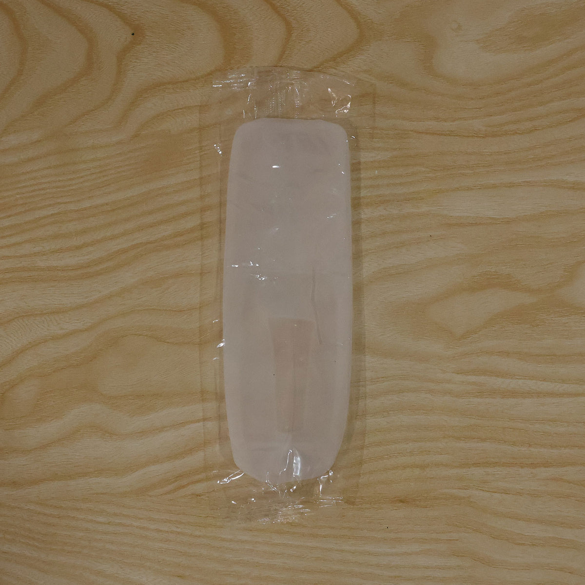 A translucent white silicone remote cover is sealed in clear plastic packaging on a light wooden surface.