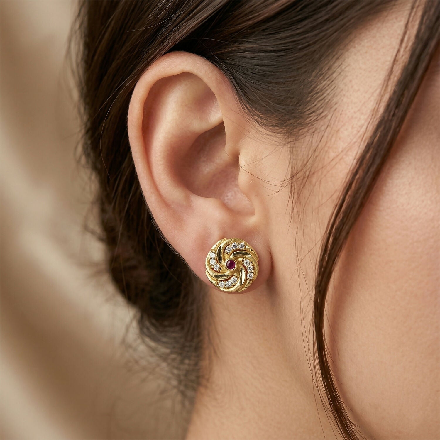 Close-up of gold spiral pattern stud earring with red stone