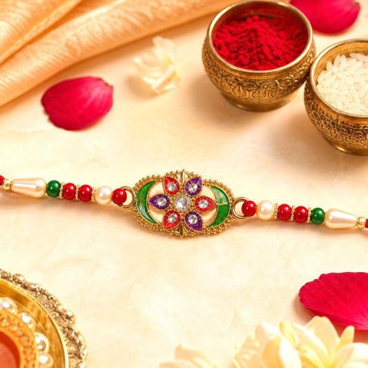 A gold-toned bracelet with a central flower design, featuring red, green, purple, and clear stones, is surrounded by red,