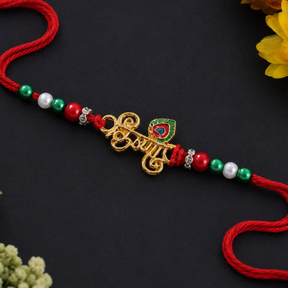 A red thread with a gold-colored charm spelling "Krishna" in Hindi, flanked by red, green, and white beads, lies on a dark