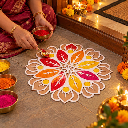 A person uses a small spoon to fill a white and brown rangoli stencil with orange powder, surrounded by bowls of various