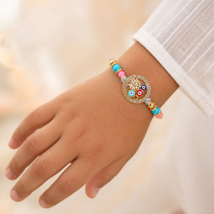 A child's hand wearing a colorful Rakhi bracelet with evil eye beads and a gold flower charm.
