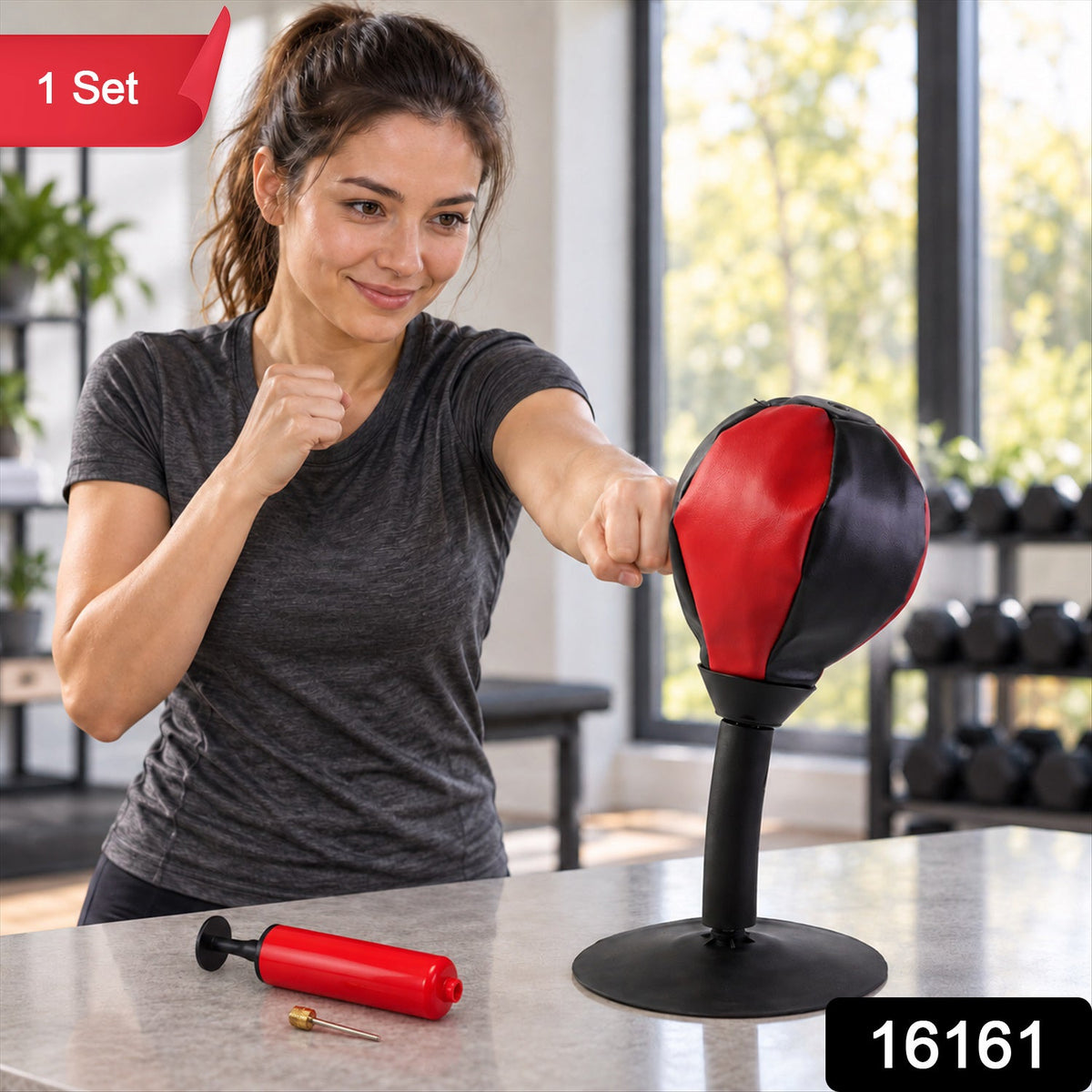 A woman in a gray shirt punches a red and black desktop punching ball on a kitchen counter, with a red hand pump nearby.