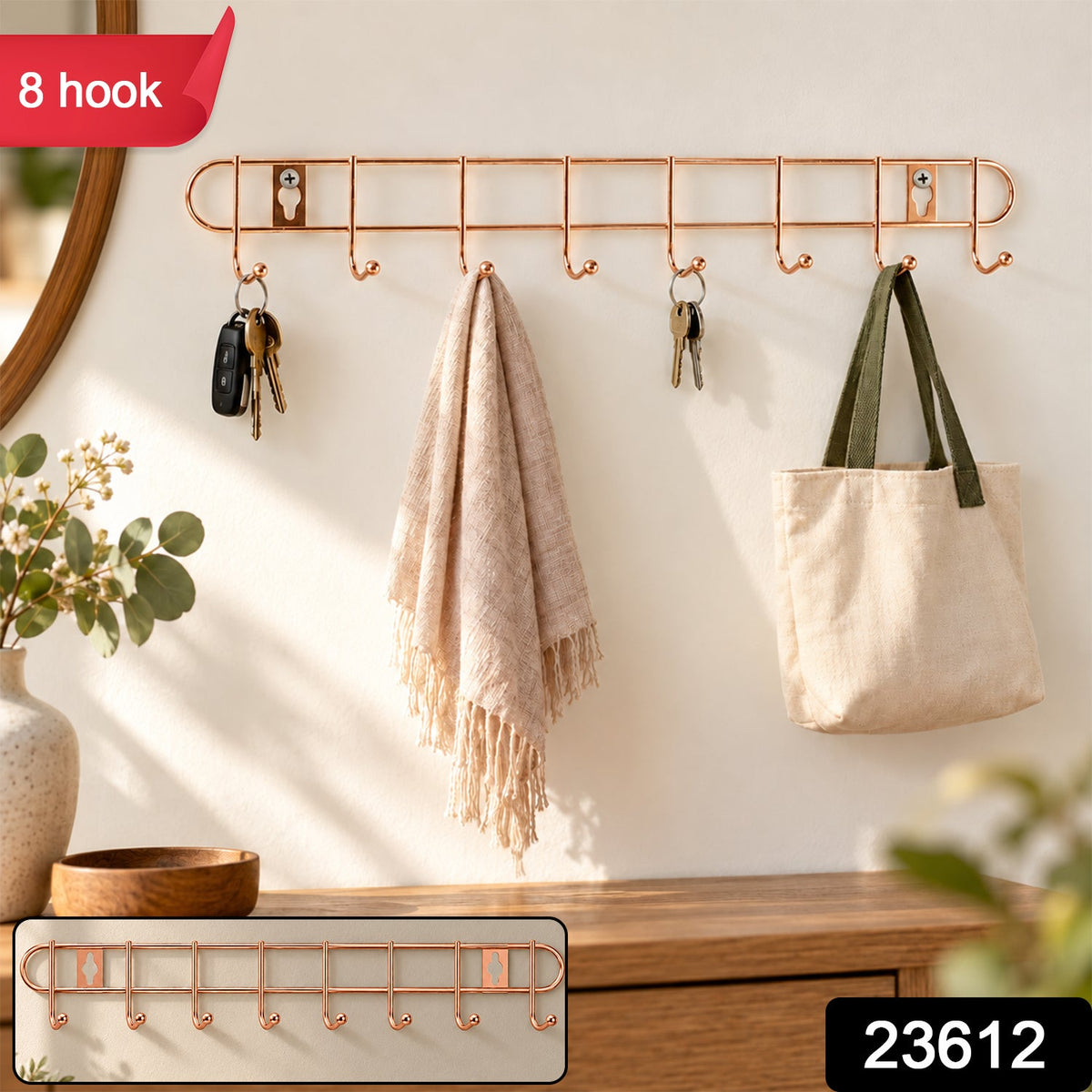 A rose gold metal wall hanger with eight hooks holds keys, a light pink towel, and a cream canvas bag, with a small inset