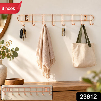 A rose gold metal wall hanger with eight hooks holds keys, a light pink towel, and a cream canvas bag, with a small inset