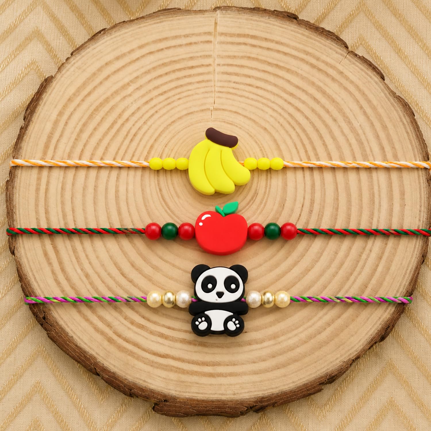 Three colorful bracelets with fruit and panda charms are displayed on a round wooden slice with a textured pattern.