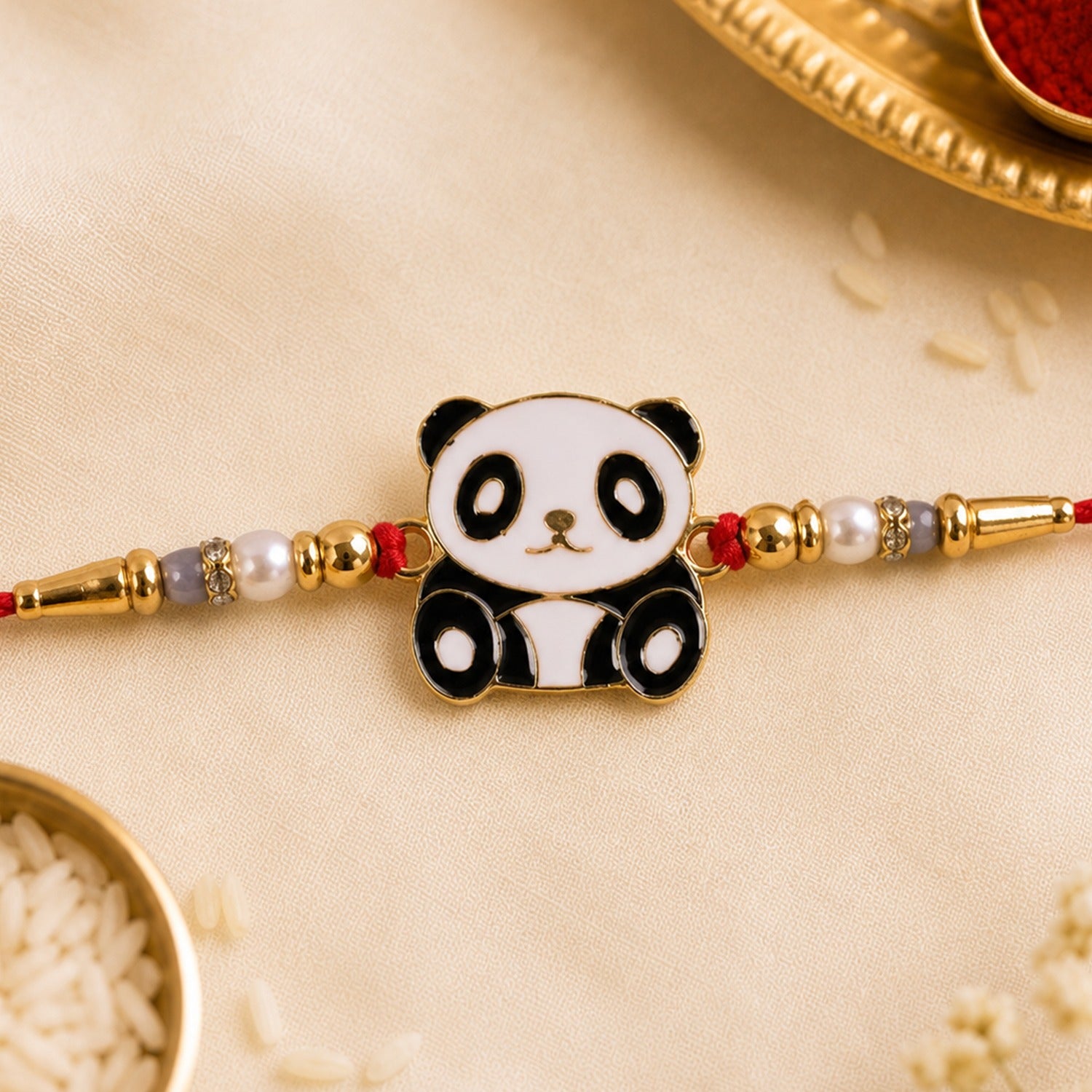 A black and white panda charm with pearl beads is centered on a red thread, surrounded by scattered rice grains.