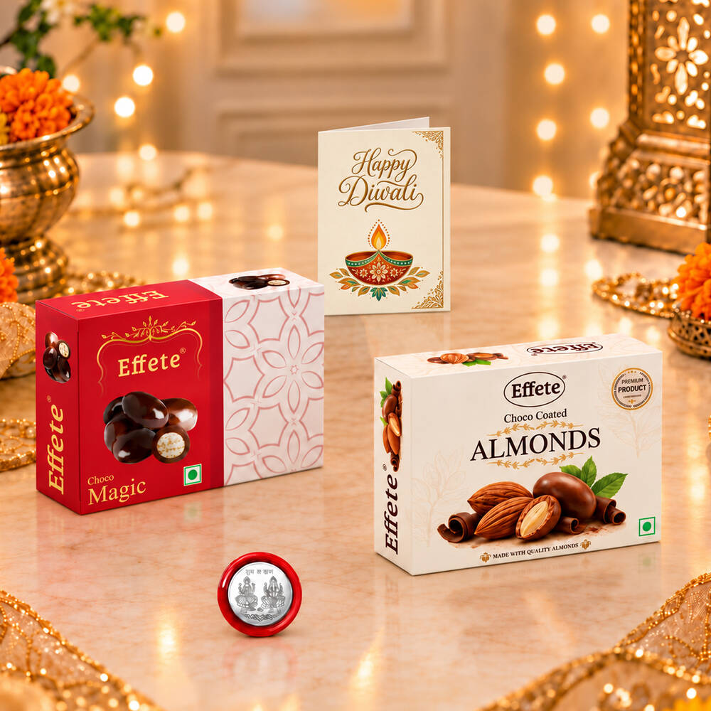 Two chocolate boxes, a silver coin, and a "Happy Diwali" card on a shiny table with blurred lights.