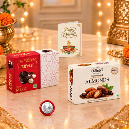 Two chocolate boxes, a silver coin, and a "Happy Diwali" card on a shiny table with blurred lights.