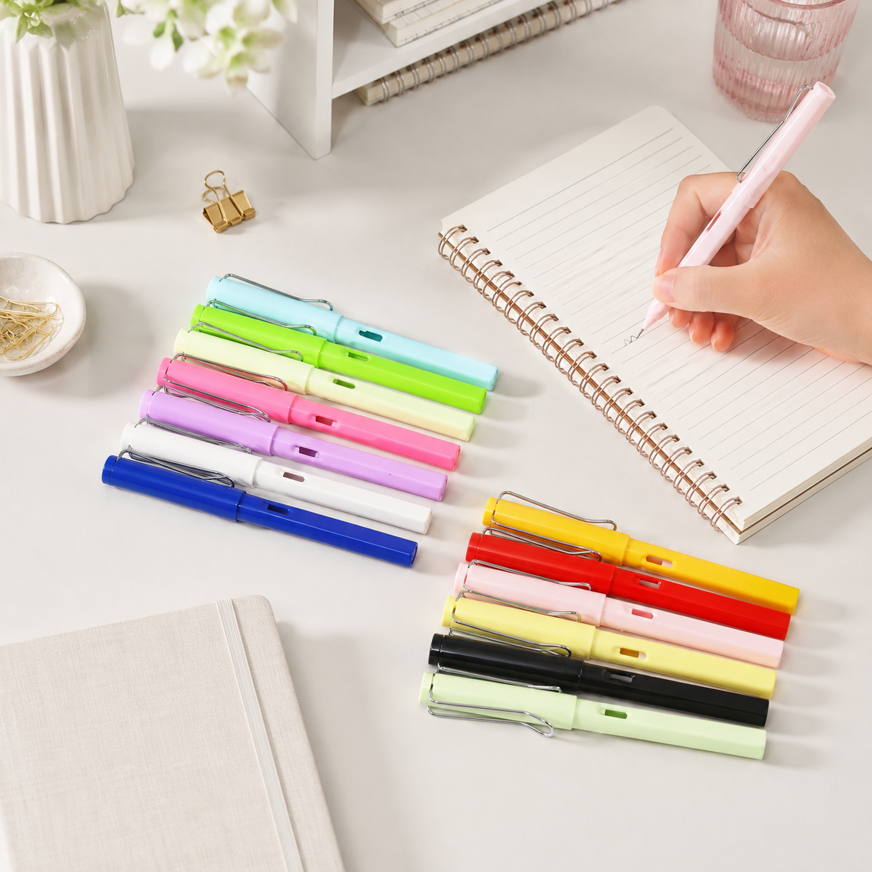 A hand writes with a pink inkless pencil on a notebook, surrounded by other colorful pencils.