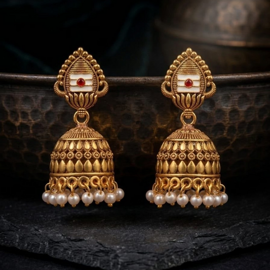 A pair of antique gold jhumka earrings with white and red enamel detailing and small pearl drops, set against a dark