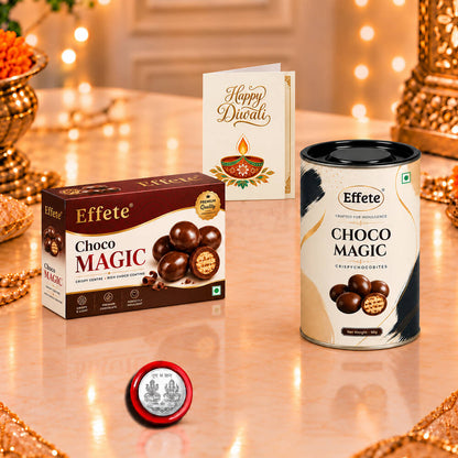 A chocolate box, canister, greeting card, and silver coin on a reflective surface with warm lights.