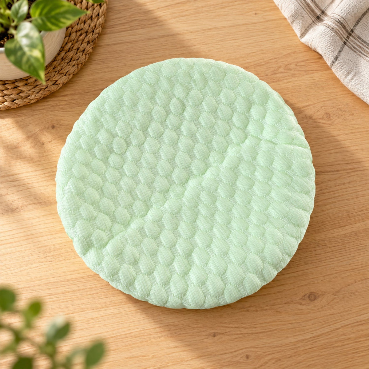 Light green textured round cushion cover with a honeycomb pattern lying flat on a wooden surface.