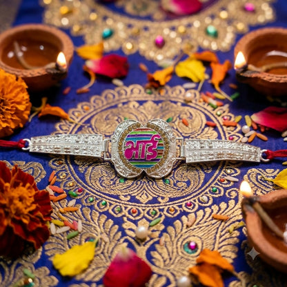 A silver-finished Bhai bracelet with a colorful center is surrounded by lit diyas, flower petals, and rice on a blue and