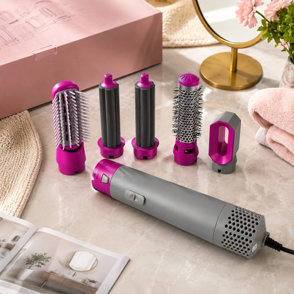 A pink and gray 5-in-1 hair styler with five attachments on a marble surface with a pink box, mirror, and towel.