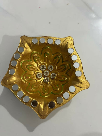 An overhead view of a golden diya featuring a central floral design with rhinestones and a mirrored edge.