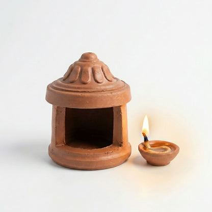 Side view of terracotta diya lamp with clay hut cover