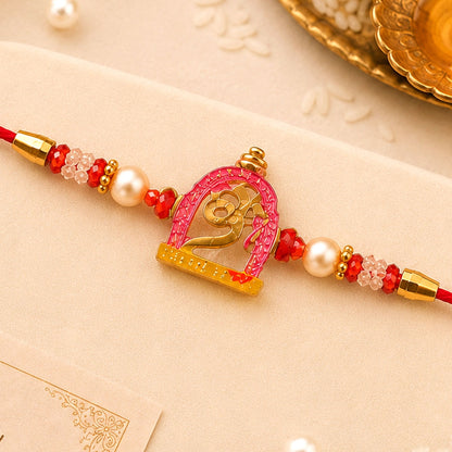 A red thread with a pink and gold Om symbol charm, flanked by white pearls and red beads, lies on a white surface.