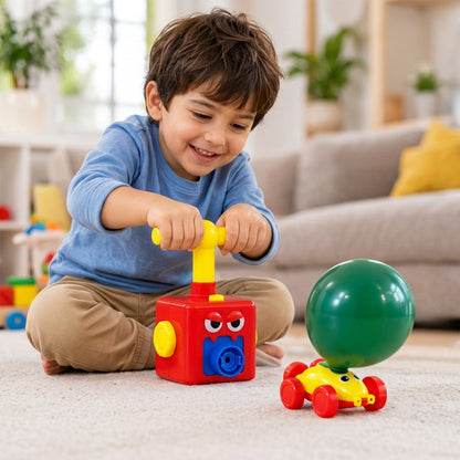 A smiling child pumps air into a green balloon attached to a yellow and red car toy.