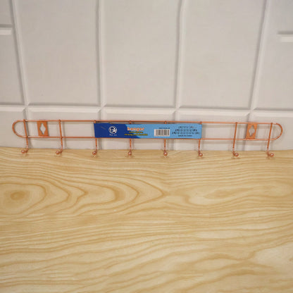 A rose gold metal wall hanger with eight hooks has a product label attached to it, resting on a light wood surface.