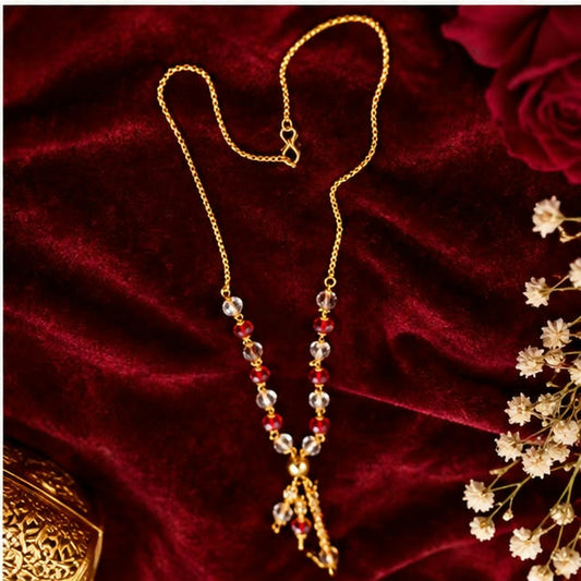 A gold chain necklace with red and clear faceted beads and a tassel pendant, displayed on a rich red velvet surface.