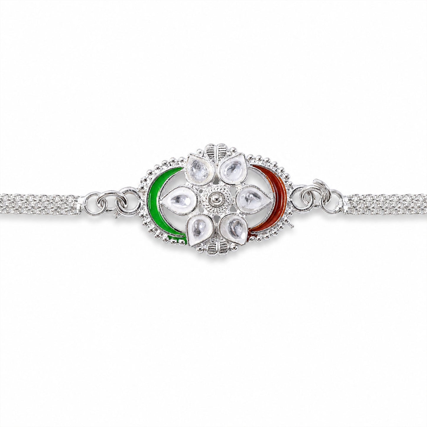 A silver rakhi with a central flower motif adorned with clear stones and green and red enamel, presented on a plain white