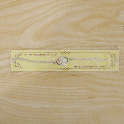 A silver rakhi with a tricolor chain link design and clear stones, packaged on a yellow card with