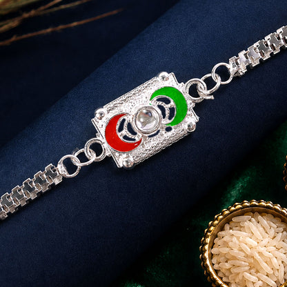 A silver-colored bracelet with a rectangular centerpiece featuring red and green crescent moon shapes, with a small bowl of