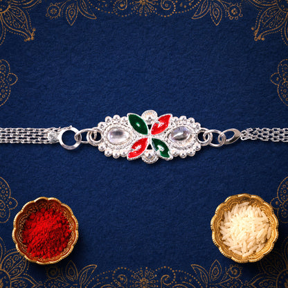 The elegant silver-toned bracelet with red and green enamel accents and clear stones rests on a dark blue background with