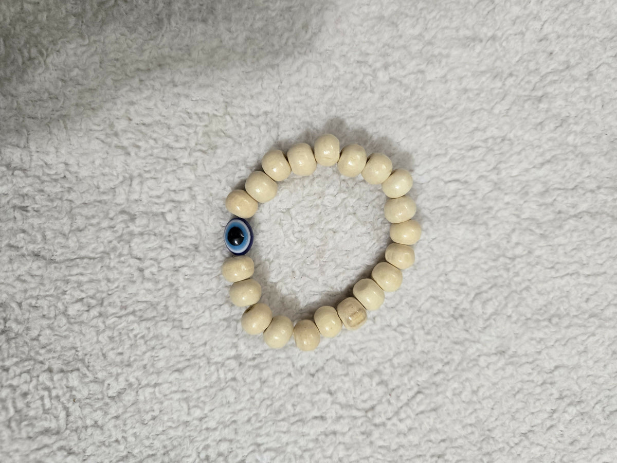 Cream barrel bead bracelet with blue evil eye on a light surface