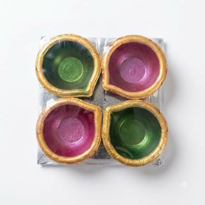 Four colorful clay diyas, two green and two magenta, with golden edges, packaged in clear plastic wrap.