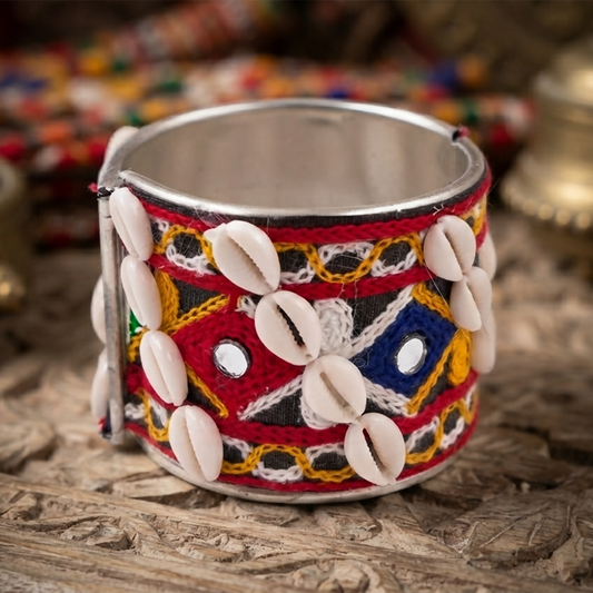 Silver cuff bangle with red, yellow, and blue thread work, adorned with small cowrie shells and tiny mirrors.