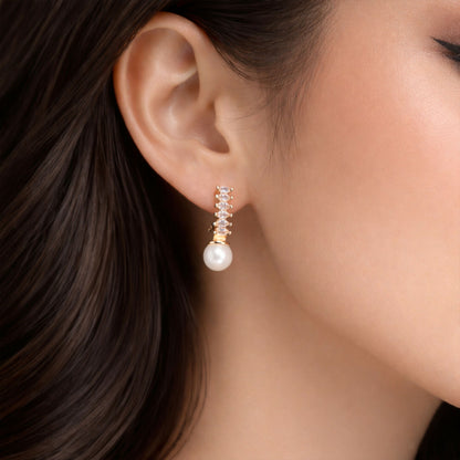 Close-up of pearl drop earrings with gold finish and shimmering stones on vertical bar