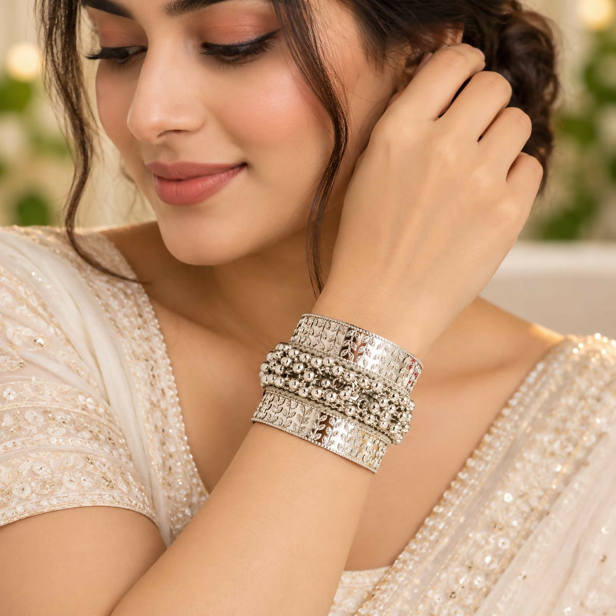 A woman with dark hair wears a silver-tone ghungroo kada bangle on her left wrist, complementing her embroidered white top.