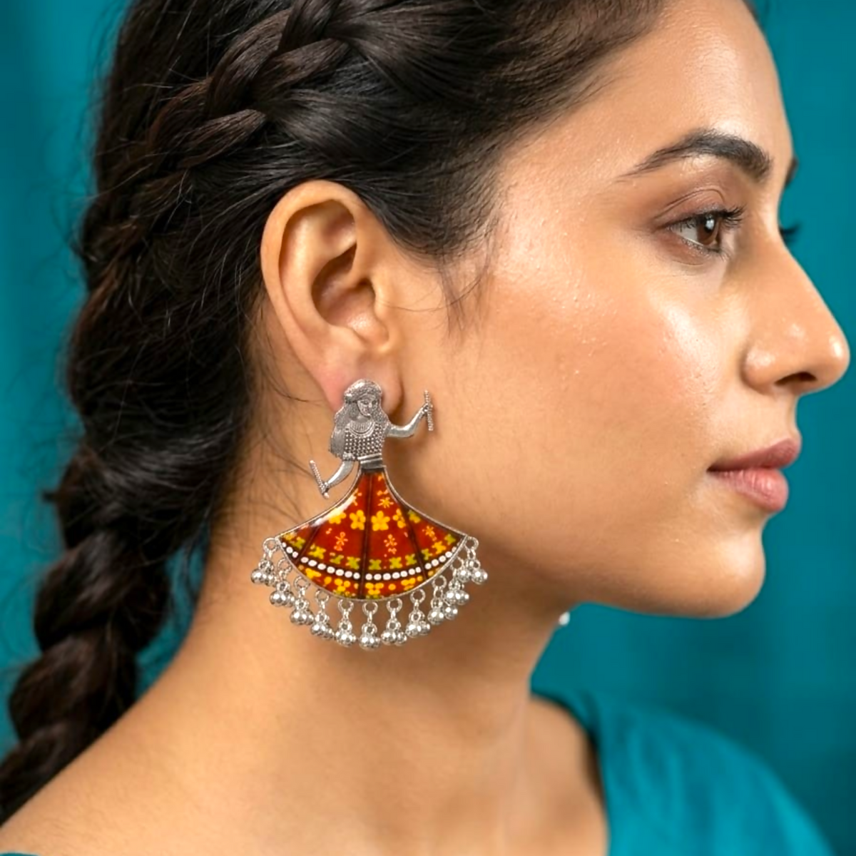 A woman models a single silver oxidized earring shaped like a dancing girl with a maroon and yellow floral skirt.