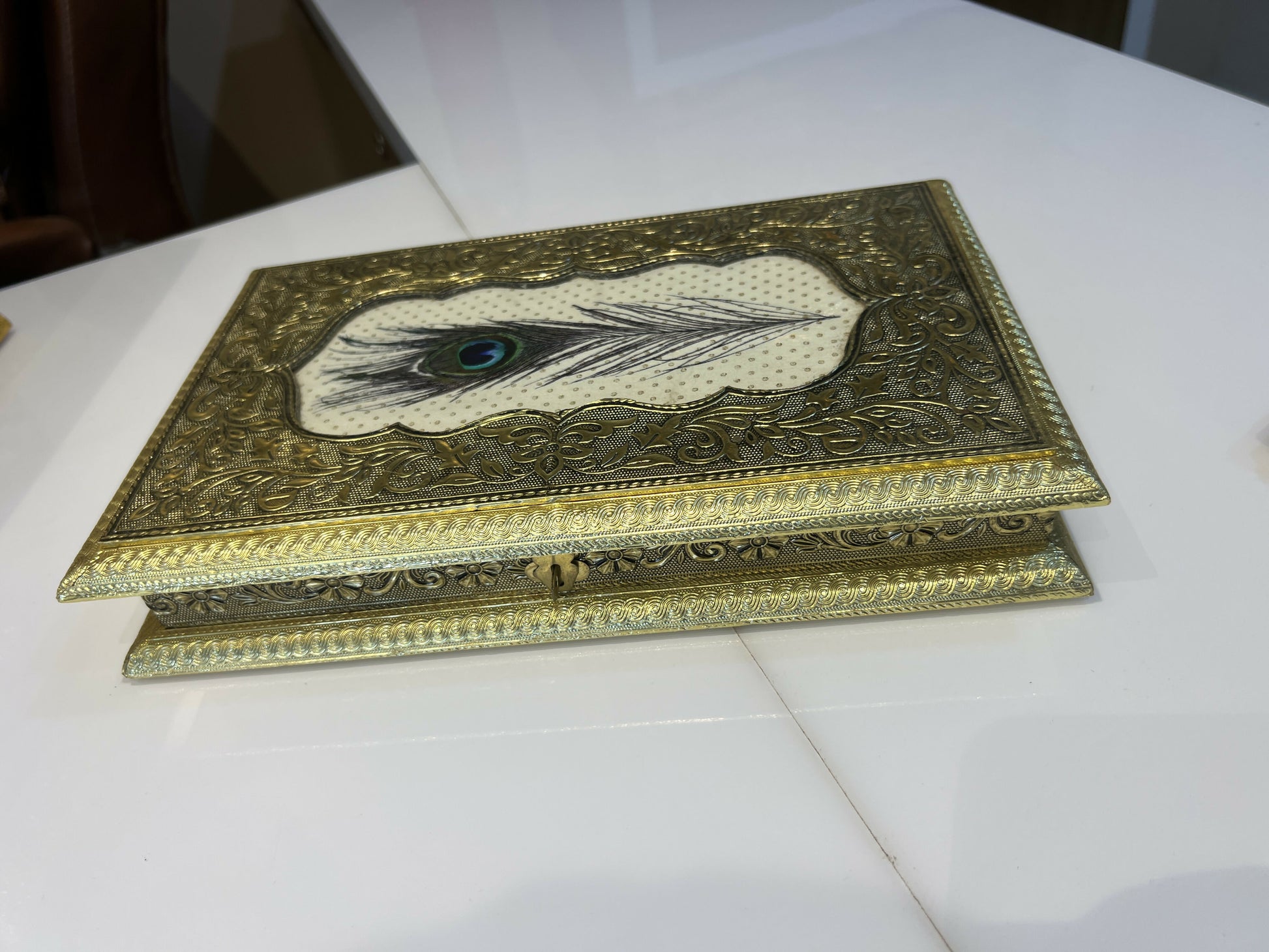 Handcrafted golden embossed peacock feather jewelry box on table, angled view