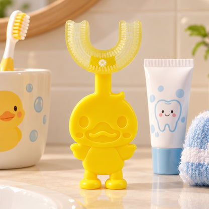 A yellow duck-shaped U-shaped toothbrush stands on a bathroom counter next to toothpaste and a cup.